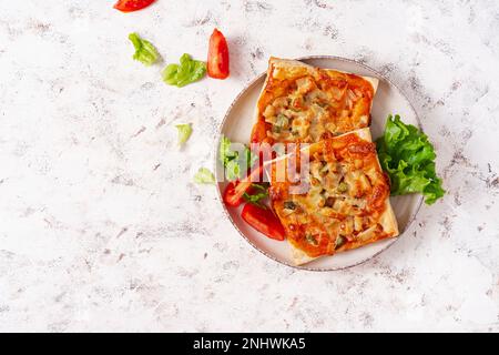 Mini pizza per bambini, piccole torte aperte con prosciutto, salsa di pomodoro, mozzarella e formaggio in cestino su sfondo chiaro. Vista dall'alto Foto Stock