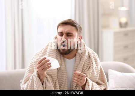 Giovane uomo che soffre di naso che cola in soggiorno Foto Stock