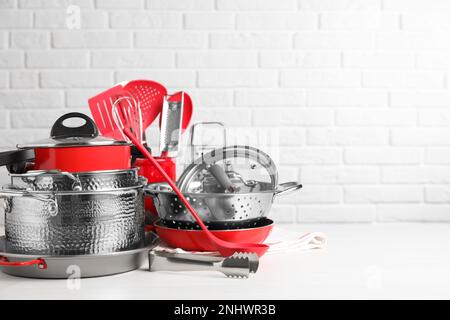 Set di utensili da cucina puliti su tavolo bianco contro muro di mattoni. Spazio per il testo Foto Stock