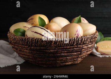 Meloni di pepino freschi maturi con foglie verdi in cestino di vimini su tavolo di legno Foto Stock