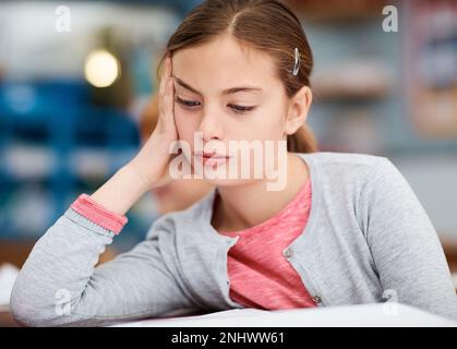 I bambini spesso lottano con la concentrazione durante i loro studi. una giovane bambina della scuola elementare che guarda annoiata mentre si siede in classe. Foto Stock