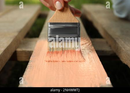 Donna che dipinge la superficie di legno con la tintura di corallo all'aperto, primo piano Foto Stock