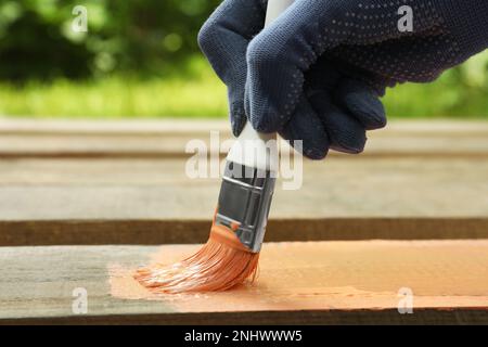 Donna che dipinge la superficie di legno con la tintura di corallo all'aperto, primo piano Foto Stock