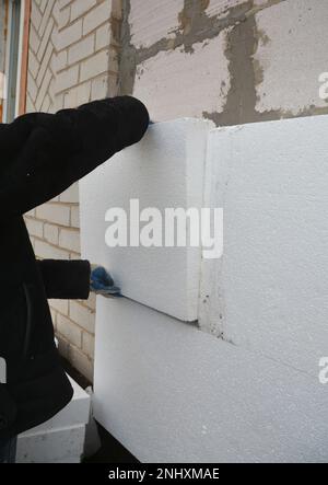 Isolamento in schiuma per pareti esterne della casa. Primo piano di un imprenditore edile che installa un isolamento in schiuma rigida e polistirolo sul blocco di calcestruzzo wal Foto Stock