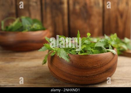 Foglie di ortica fresca pungente in una ciotola su un tavolo di legno Foto Stock