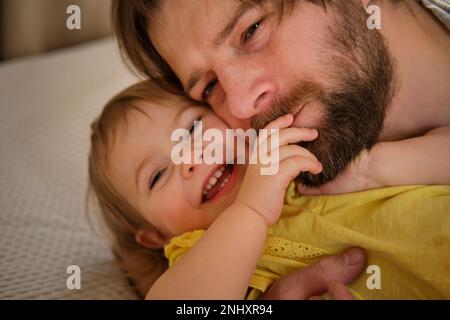 Padre felice con figlia, ragazza piccola. Un anno Bambino sorridente, Laughing, guardando in su a Daddy. L'uomo che mostra affetto al Bambino. Sincero vera emozione. Orso Foto Stock
