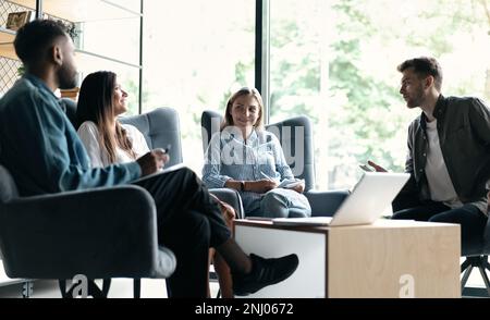 Colleghi felici e interessati seduti sulle sedie, ascoltando il capo del team, spiegando i problemi di lavoro durante la riunione Foto Stock