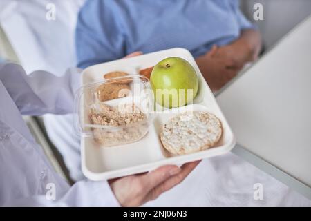 Primo piano dell'infermiera che tiene un pasto sano della colazione sul vassoio e che porta dentro al paziente in ospedale Foto Stock