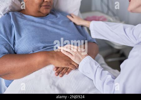 Primo piano di una giovane infermiera che sostiene la paziente femminile nel letto di ospedale Foto Stock