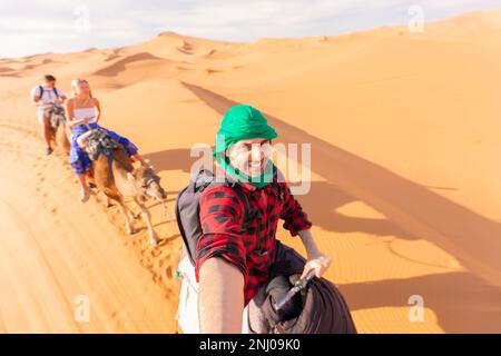 Uomo che si diverte con il gruppo mentre cavalca il cammello nel deserto Foto Stock