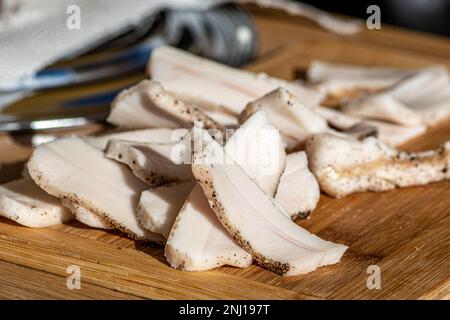 Pezzi di strutto o pancetta, affettati sottilmente per il consumo, su un tagliere di legno in un mercato di cibo di strada, primo piano Foto Stock