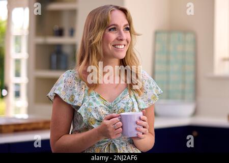 Donna sorridente in piedi in cucina rilassante con tazza di caffè Foto Stock