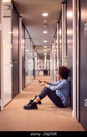 Stressato giovane Businesswoman seduto sul pavimento in corridoio di Ufficio moderno con Telefono Foto Stock