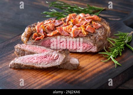 Bistecca di manzo tagliata a fette con pancetta sbriciolata guarnita con rosmarino Foto Stock