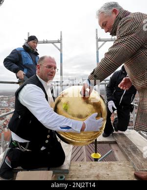 Wismar, Germania. 22nd Feb, 2023. Su una delle due guglie di St. Nikolai, Sven Knaebe, maestro artigiano del Neumühler Bauhütte, detiene una delle due guglie dorate in cui Thomas Beyer (SPD), sindaco, inserisce capsule temporali contenenti documenti di eventi contemporanei. L'esteso lavoro di ristrutturazione del sacro edificio tardo gotico, che è stato costruito nel 15th ° secolo come una chiesa per i marinai e pescatori e ancora forma la silhouette della città anseatica, ha avuto inizio quattro anni fa. Credit: Bernd Wüstneck/dpa/Alamy Live News Foto Stock