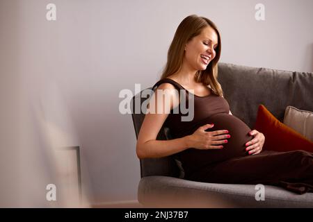 Donna incinta che si rilassa su divano a casa Holding stomaco Foto Stock
