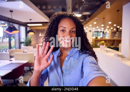 POV Selfie Ritratto di Waving Businesswoman in piedi in Modern Open Plan Office Foto Stock