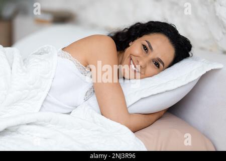 Felice donna caucasica millenaria svegliarsi e si trova su un morbido cuscino, godersi la buona mattina, riposo e relax Foto Stock