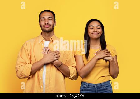 Allegro giovane afro-americano ragazzo e donna con gli occhi chiusi mettere le mani al petto, grazie Foto Stock