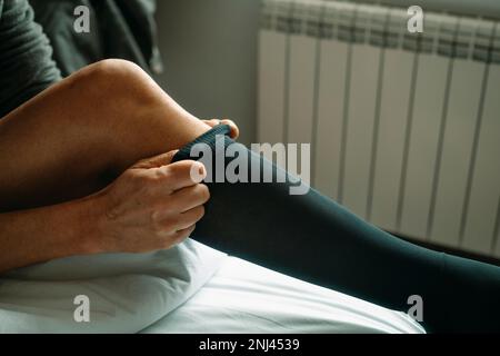 primo piano di un uomo che si mette su una calza a compressione seduta sul letto a casa Foto Stock