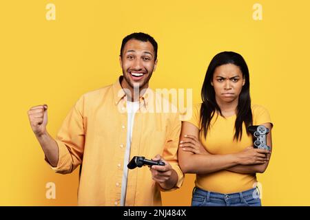 Felice giovane ragazzo nero e offeso triste arrabbiato moglie con joystick divertirsi insieme, giocando a videogame per computer Foto Stock