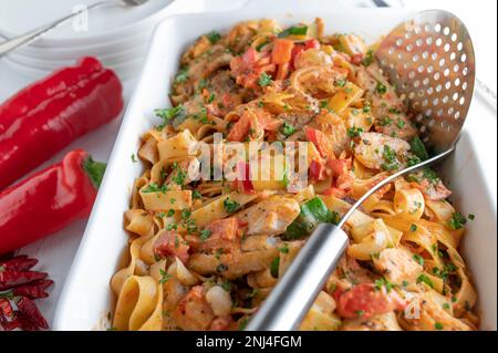 Pesce con pasta e verdure mediterranee in un piatto da forno bianco Foto Stock