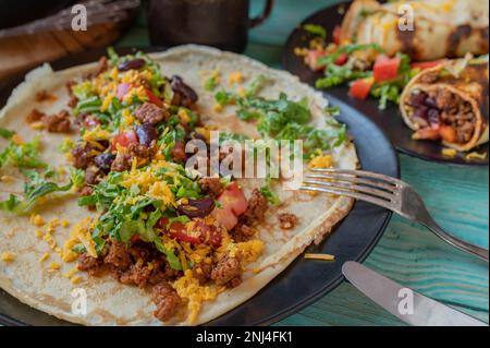 Aprire il burrito con carne macinata, fagioli rossi, formaggio cheddar, pomodori e lattuga su un piatto Foto Stock