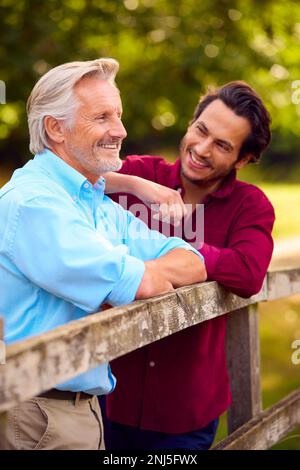 Padre maturo con razza mista Figlio adulto che pende su Fence Walking in campagna Foto Stock