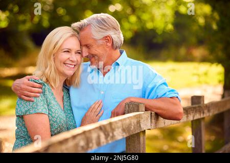 Amorevole coppia matura o anziana vestita casualmente appoggiata su Fence a piedi in campagna Foto Stock