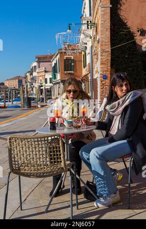 Due donne che hanno un antipasto aperol Spritz al sole a Murano, Venezia, Italia nel mese di febbraio Foto Stock