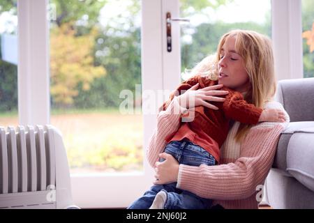 Madre con il Figlio cercando di mantenere caldo da radiatore a casa durante il costo di vivere crisi di energia Foto Stock