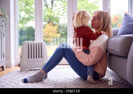 Madre con il Figlio cercando di mantenere caldo da radiatore a casa durante il costo di vivere crisi di energia Foto Stock