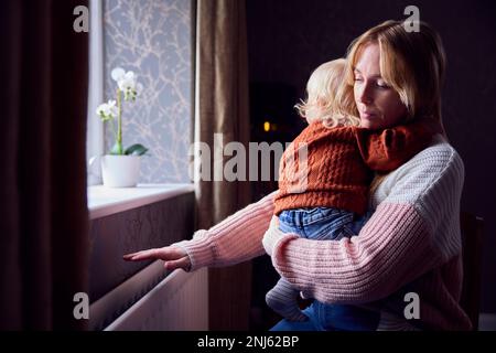 Madre con il Figlio cercando di mantenere caldo da radiatore a casa durante il costo di vivere crisi di energia Foto Stock