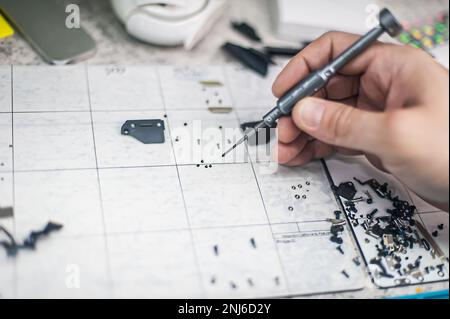 Vista dall'alto del luogo di lavoro, primo piano. Il riparatore smonta lo smartphone con un cacciavite in un negozio di riparazione elettronica. Foto Stock