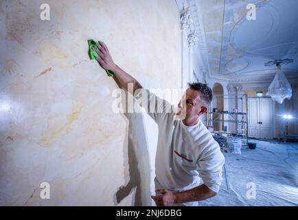 22 febbraio 2023, Meclemburgo-Pomerania occidentale, Ludwigslust: Una replica del muro di marmo è lucidata con cera da Dirk Westphal della società Guse Stuck und Restaurierung nella sala di marmo del castello di Ludwigslust. Lo stato di Meclemburgo-Pomerania occidentale ha finora investito circa 35 milioni di euro nel castello, che è stato costruito tra il 1772 e il 1776, dal 1992, rendendo possibile un ampio restauro dell'edificio. Fino alla primavera del 2024, l'ala ovest sarà rinnovata con oltre 19 milioni di euro. Oltre al rinforzo strutturale, l'interno storico con lampadari, specchi, fuoco Foto Stock