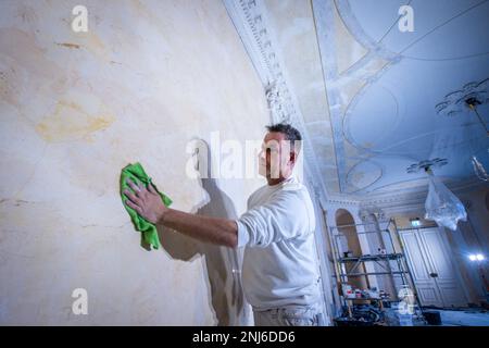 22 febbraio 2023, Meclemburgo-Pomerania occidentale, Ludwigslust: Una replica del muro di marmo è lucidata con cera da Dirk Westphal della società Guse Stuck und Restaurierung nella sala di marmo del castello di Ludwigslust. Lo stato di Meclemburgo-Pomerania occidentale ha finora investito circa 35 milioni di euro nel castello, che è stato costruito tra il 1772 e il 1776, dal 1992, rendendo possibile un ampio restauro dell'edificio. Fino alla primavera del 2024, l'ala ovest sarà rinnovata con oltre 19 milioni di euro. Oltre al rinforzo strutturale, l'interno storico con lampadari, specchi, fuoco Foto Stock