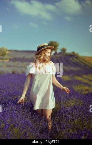 Bella ragazza sul campo di lavanda. Bella donna nel campo di lavanda al tramonto. Messa a fuoco soft. Provenza, Francia. Una ragazza in abito rosa e cappello a piedi Foto Stock