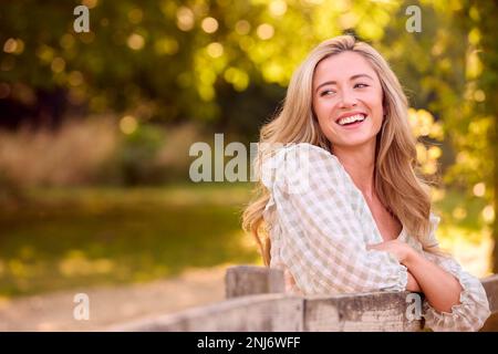 Giovane donna vestita casualmente appoggiata su Fence a piedi in campagna Foto Stock