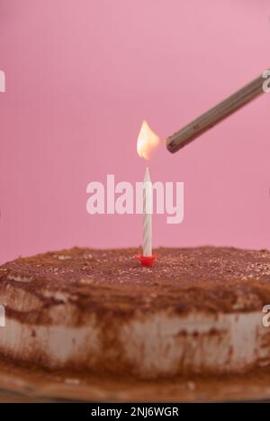 Torta di compleanno o anniversario con una candela accesa con un accendino su una torta decorata con cioccolato. Immagine con spazio di copia Foto Stock