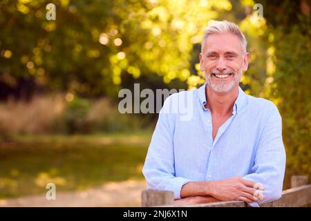 Ritratto di uomo maturo vestito casualmente Pendente su Fence a piedi in campagna Foto Stock