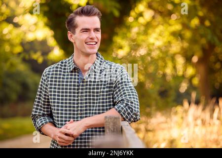 Uomo vestito casualmente che si appoggia su Fence a piedi in campagna Foto Stock