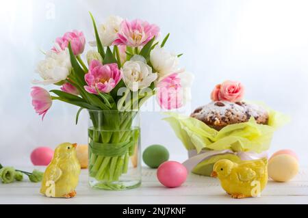 Bouquet pasquale di tulipani primaverili con torta pasquale, uova e decorazioni festive su tavolo di legno bianco. Concetto di Pasqua con spazio di copia. Foto Stock