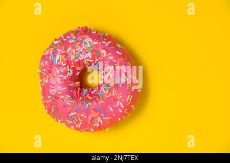 Ciambella con glassa rosa e zuccherini multicolore. Su fondo giallo Foto Stock