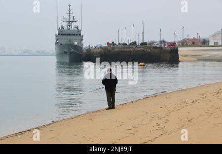 Un uomo in piedi sulla canna da spiaggia e la pesca con lenza e la nave di pattuglia spagnola Serviola P-71 ormeggiato nella zona del porto di Gamaso di Santander Bay Cantabria Spagna Foto Stock