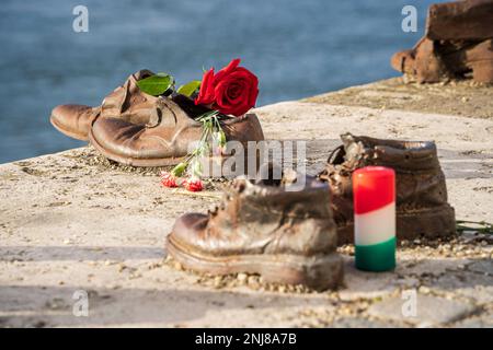 Scarpe sulla riva del Danubio, Budapest, Ungheria. Memoriale agli ebrei ungheresi, vittime dell'Olocausto. Rosa rossa e candela. Primo piano. Budapest, Ungheria - 2 febbraio 2023. Foto Stock