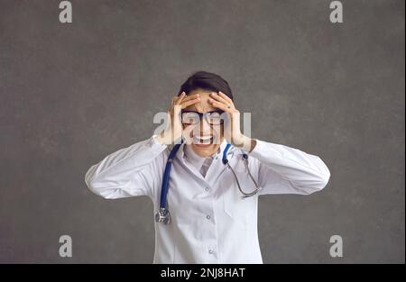 L'infermiera o il medico dell'ospedale stressato scoppia in lacrime isolate su uno sfondo grigio Foto Stock