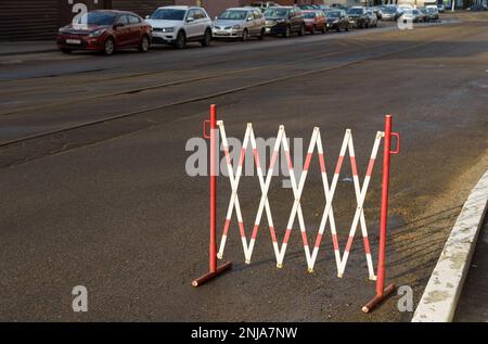 Recinzione temporanea restrittiva di colore rosso e bianco in un'area di parcheggio su una strada cittadina. Foto Stock