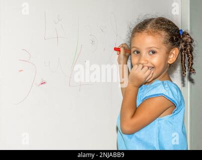 Piccola ragazza brasiliana che scarabocchio, dipinge e disegna su una parete di colore giallo chiaro Foto Stock