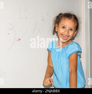 Piccola ragazza brasiliana che scarabocchio, dipinge e disegna su una parete di colore giallo chiaro Foto Stock