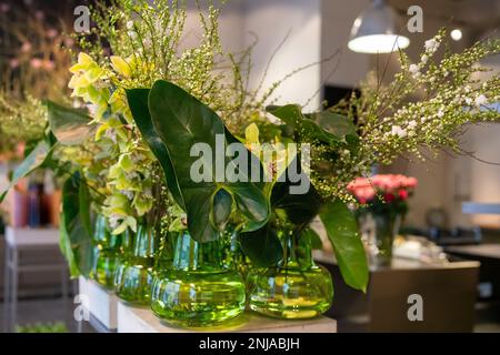 Vasi decorativi in vetro con fiori. Green Philodendron Burle-marxii e Gloriosa superba in primo piano. Foto Stock